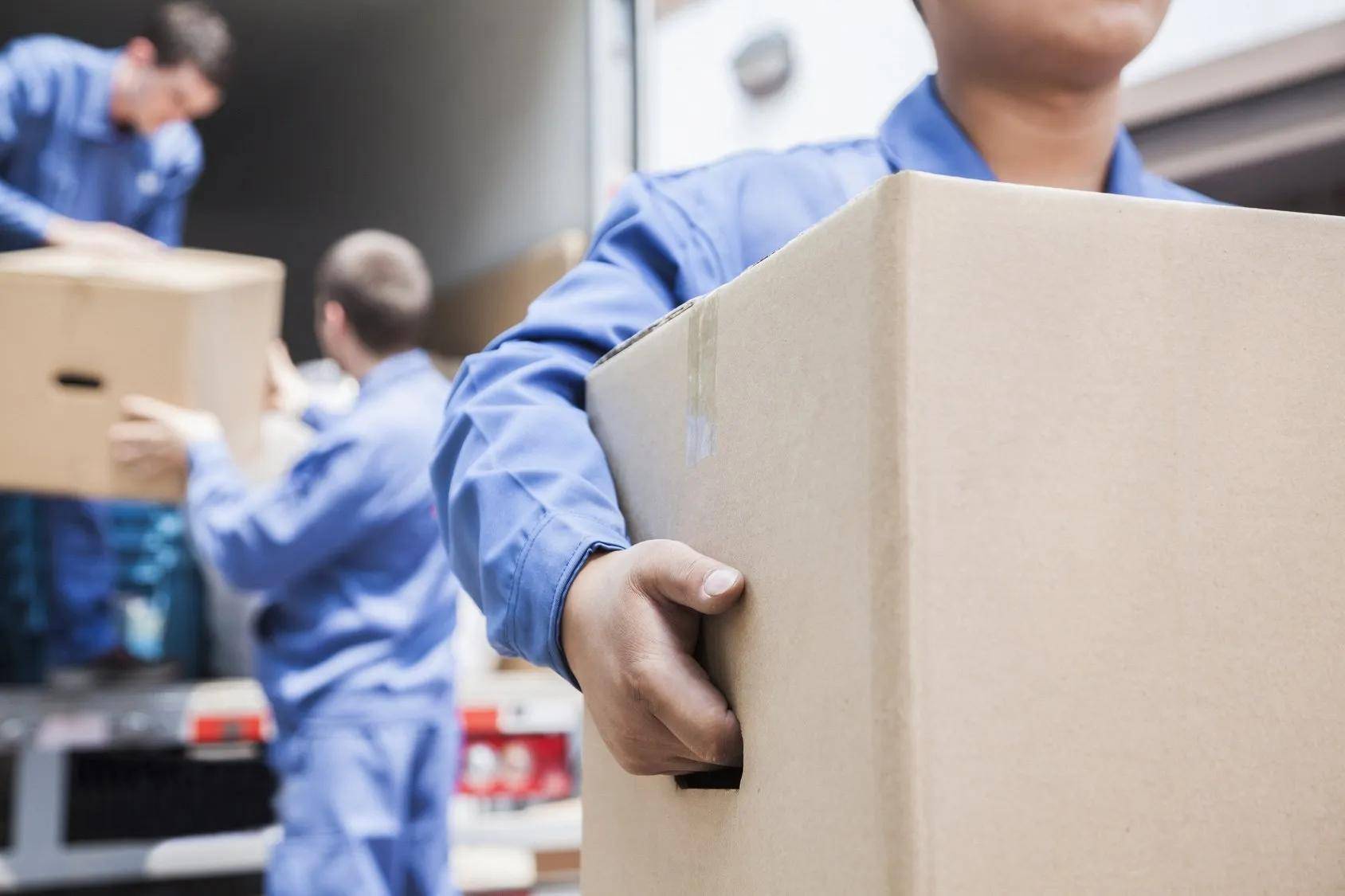 A man is carrying a cardboard box in front of a truck.